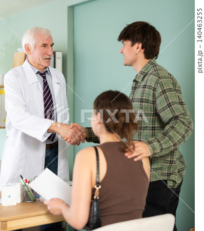 In clinics office, senior male doctor shakes hands with young couple patients 140463255