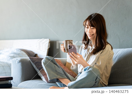 リビングのソファに座ってスマートフォンを使う女性 リビングのソファに座ってスマートフォンを使う女性 140463275
