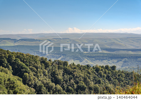 Panoramic view of the green valley and the snowy peak of Mount Elbrus on the horizon against the blue sky on a sunny clear morning in Kislovodsk Stavropol territory, Russia Panoramic view of the green valley and the snowy peak of Mount Elbrus on the horizon against the blue sky on a sunny clear morning in Kislovodsk Stavropol territory, Russia 140464044