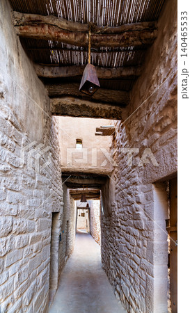 A narrow passage through the historic stone buildings of AlUla Old Town featuring traditional architectural details and hanging lanterns in Saudi Arabia. A narrow passage through the historic stone buildings of AlUla Old Town featuring traditional architectural details and hanging lanterns in Saudi Arabia. 140465533