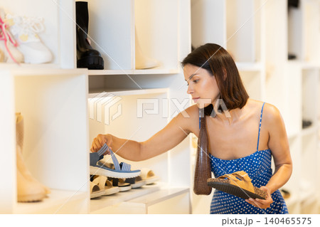 Girl customer chooses sandals in store, and buyer carefully examines product. Girl customer chooses sandals in store, and buyer carefully examines product. 140465575