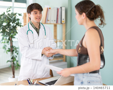 Male doctor shaking hands with young female patient at table Male doctor shaking hands with young female patient at table 140465711