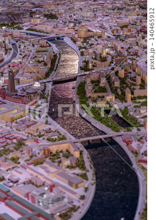 Detailed display of a city model featuring buildings, bridges, and flowing rivers in a lively urban environment under bright daylight. Detailed display of a city model featuring buildings, bridges, and flowing rivers in a lively urban environment under bright daylight. 140465912
