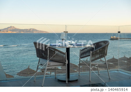 Luxury seaside dining at sunset, with beautifully arranged tables and shimmering glassware reflecting ocean waves Luxury seaside dining at sunset, with beautifully arranged tables and shimmering glassware reflecting ocean waves 140465914
