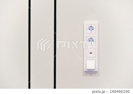 Two power outlets and one switch are mounted on a light wall surface in a contemporary indoor area featuring simple design. Two power outlets and one switch are mounted on a light wall surface in a contemporary indoor area featuring simple design. 140466100