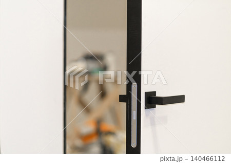 A close view of a door handle being installed in a renovated home. Tools and materials are visible in the background. A close view of a door handle being installed in a renovated home. Tools and materials are visible in the background. 140466112