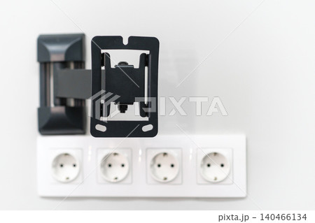 A wall mount holder is placed above several electrical outlets in a bright indoor area, showcasing a tidy and organized setup. 140466134