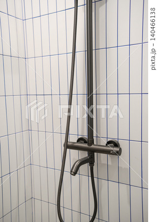 Shower fixture mounted on white tiled wall with blue grout lines in a bright bathroom space during daylight hours. 140466138