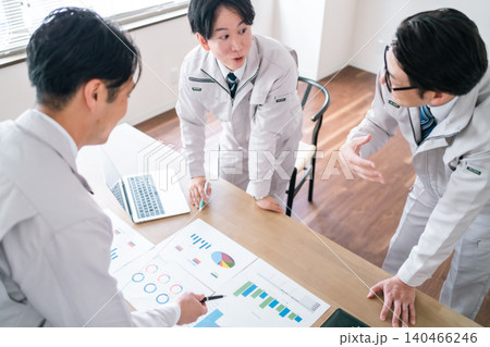 会議室で資料を見ながら笑顔で談笑する作業着姿の男性会社員3人 会議室で資料を見ながら笑顔で談笑する作業着姿の男性会社員3人 140466246