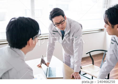 会議室で資料を見ながら熱くプロジェクトについて語る作業着姿の男性会社員3人 会議室で資料を見ながら熱くプロジェクトについて語る作業着姿の男性会社員3人 140466250