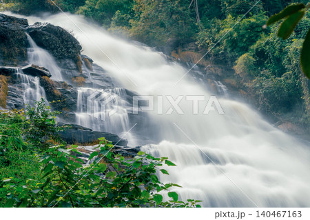 Beautiful waterfall with a lush green forest in the background. The water is flowing down the rocks and creating a beautiful scene. Sustainable waterfall in lush forest promoting water sustainability. Beautiful waterfall with a lush green forest in the background. The water is flowing down the rocks and creating a beautiful scene. Sustainable waterfall in lush forest promoting water sustainability. 140467163