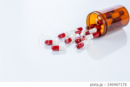 Red and white prescription capsules spilling from a plastic container. Regulated pharmaceutical drugs. Emphasizing safety standards, medication efficacy, and patient well-being in healthcare industry. Red and white prescription capsules spilling from a plastic container. Regulated pharmaceutical drugs. Emphasizing safety standards, medication efficacy, and patient well-being in healthcare industry. 140467178