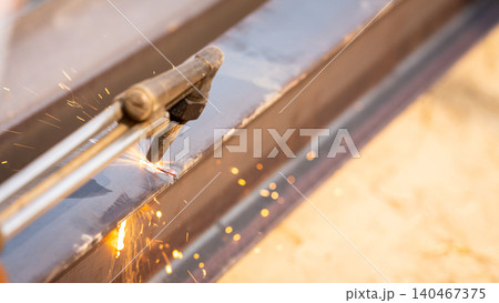 Skilled metalworker uses torch to cut through steel. Sparks fly as craftsman demonstrates precision in industrial workshop. Concept of balancing risk and expertise in dangerous metalworking processes. 140467375