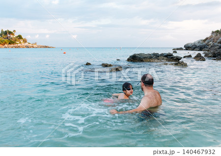 high angle view of a dad and a daughter swimming together in blue sea 140467932