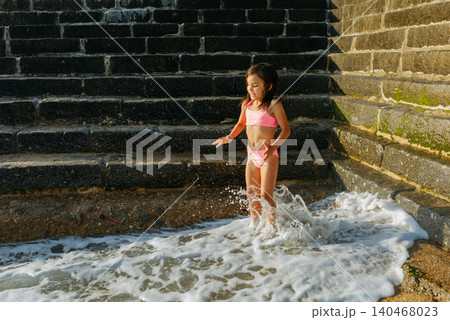 happy small girl jumping in the waves next to the wall happy small girl jumping in the waves next to the wall 140468023