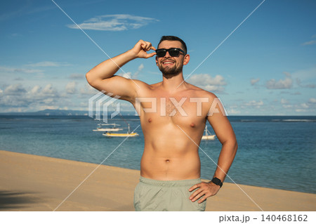 Man smiles and poses at the beach with blue water and sky 140468162