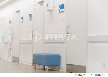 A hallway features multiple closed doors with a blue bench placed against the wall, creating a typical indoor scene in a building. A hallway features multiple closed doors with a blue bench placed against the wall, creating a typical indoor scene in a building. 140468285