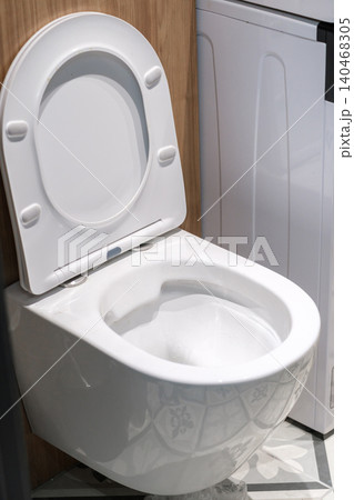 A white toilet is located next to a laundry machine in a modern bathroom with patterned floor tiles and a wooden wall. 140468305