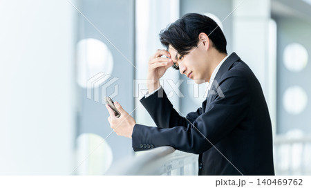 スマートフォンを見て悩む男性ビジネスマン スマートフォンを見て悩む男性ビジネスマン 140469762