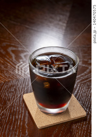 ダーク木目テーブルのコルクコースターに置いたアイスコーヒーの縦位置写真 140470575