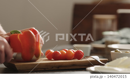 Close-up of red bell pepper being sliced on wooden cutting board with cherry tomatoes Close-up of red bell pepper being sliced on wooden cutting board with cherry tomatoes 140472015