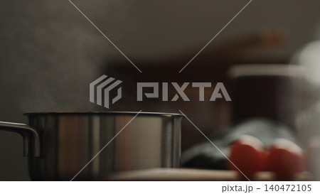 Stainless steel pot steaming on kitchen stovetop with tomatoes nearby 140472105