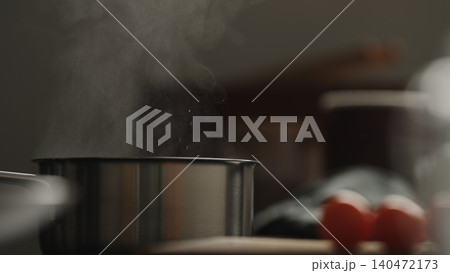 Stainless steel pot steaming on kitchen stovetop with tomatoes nearby Stainless steel pot steaming on kitchen stovetop with tomatoes nearby 140472173