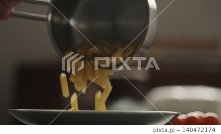 penne pasta falls from saucepan in white plate 140472174