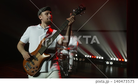 Musician performing bass guitar on stage with dramatic red lighting Musician performing bass guitar on stage with dramatic red lighting 140473575