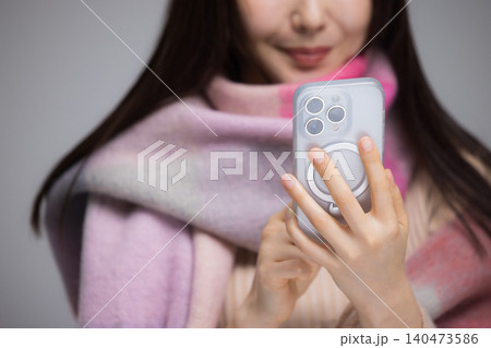 マフラーを巻き、携帯電話を使う若い女性 マフラーを巻き、携帯電話を使う若い女性 140473586