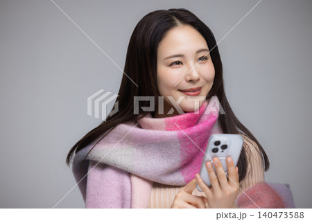 マフラーを巻き、携帯電話を使う若い女性 マフラーを巻き、携帯電話を使う若い女性 140473588