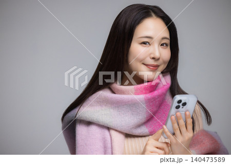 マフラーを巻き、携帯電話を使う若い女性 マフラーを巻き、携帯電話を使う若い女性 140473589
