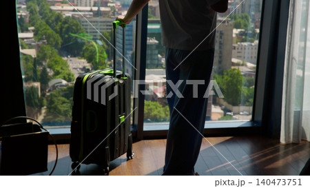 Traveler with luggage gazing at cityscape from high rise hotel window Traveler with luggage gazing at cityscape from high rise hotel window 140473751