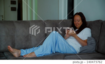 Woman relaxing on gray couch using smartphone at home Woman relaxing on gray couch using smartphone at home 140473762