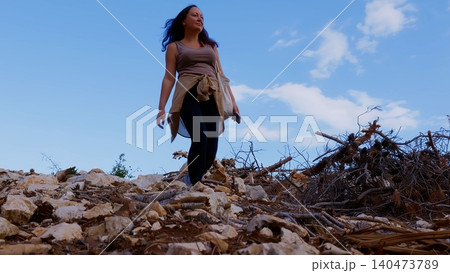 Woman hiking through rocky terrain with dead wood, blue sky 140473789