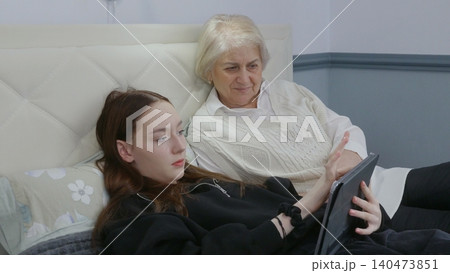 Senior woman, teen girl viewing tablet together on couch Senior woman, teen girl viewing tablet together on couch 140473851