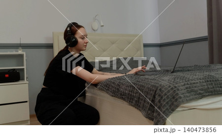Woman wearing headphones dancing on bedroom bed Woman wearing headphones dancing on bedroom bed 140473856