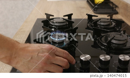 Person lighting gas burner on stovetop with ignition flame 140474015