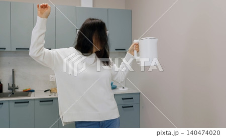 Woman celebrating with raised fist holding coffee mug in modern kitchen 140474020