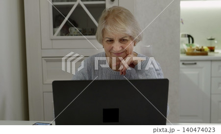 Senior woman using laptop at home kitchen table 140474023