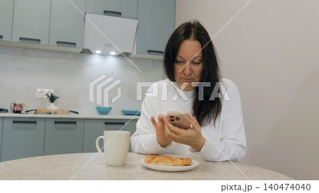 Woman using smartphone during breakfast in modern kitchen Woman using smartphone during breakfast in modern kitchen 140474040