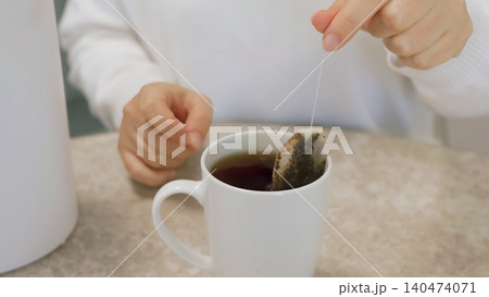 Person steeping tea bag in hot water inside white mug 140474071