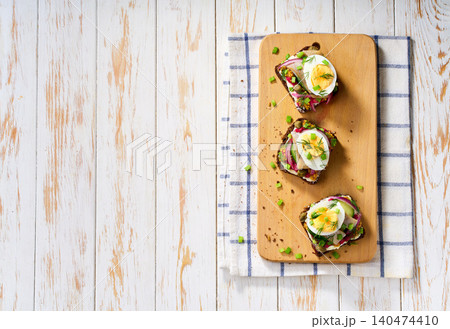 Smorrebrod, a traditional Danish open sandwich on dark rye bread with herring, pickled beets and boiled eggs, capers, red onion on white table, top view. Smorrebrod, a traditional Danish open sandwich on dark rye bread with herring, pickled beets and boiled eggs, capers, red onion on white table, top view. 140474410
