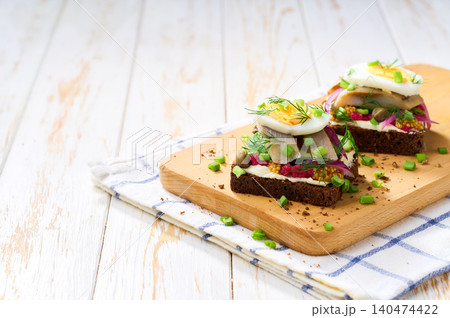 Sandwiches with rye bread, slices of herring fillet, red onion , beetroot,cucumber, on a white wooden table. A traditional light scandinavian snack . Sandwiches with rye bread, slices of herring fillet, red onion , beetroot,cucumber, on a white wooden table. A traditional light scandinavian snack . 140474422