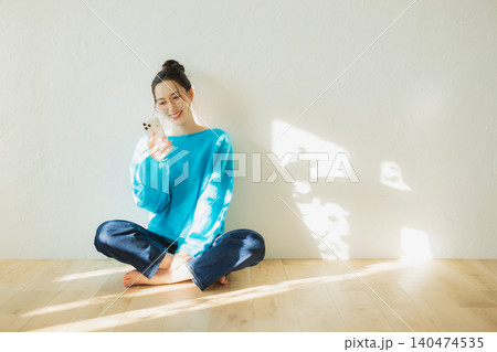 床に座ってスマホを見る若い女性　　 140474535