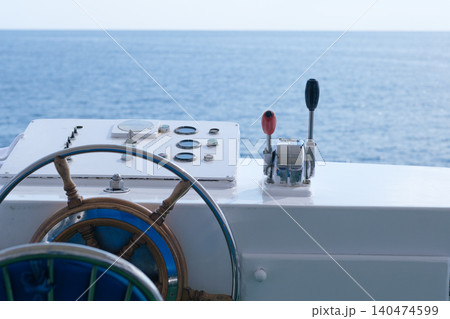 Boat steering wheel and control panel featuring gauges, positioned against a backdrop of calm ocean waters under a clear sky 140474599