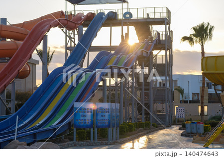 Colorful water slides are visible at an amusement park, with multiple levels and a sunset illuminating the scene against a clear sky Colorful water slides are visible at an amusement park, with multiple levels and a sunset illuminating the scene against a clear sky 140474643