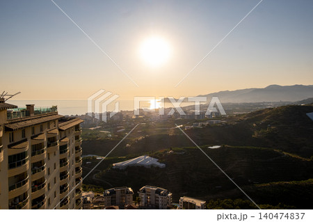 Beautiful golden sunset illuminates a coastal city, with buildings in the foreground and mountains rising in the distance along the serene water. Beautiful golden sunset illuminates a coastal city, with buildings in the foreground and mountains rising in the distance along the serene water. 140474837