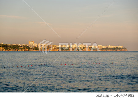 Overlooking tranquil waters, a coastal city skyline glows in the warm light of sunset, showcasing buildings against a clear sky. Overlooking tranquil waters, a coastal city skyline glows in the warm light of sunset, showcasing buildings against a clear sky. 140474982