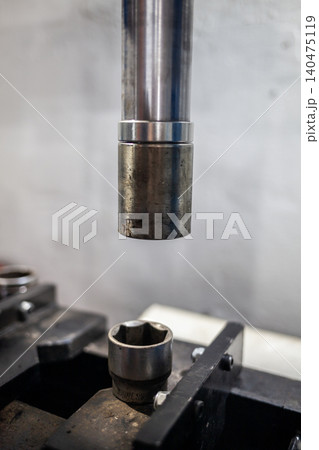 A metal rod hovers above a socket tool, showcasing precision mechanics in a workshop, as workers engage in detailed metal fabrication. A metal rod hovers above a socket tool, showcasing precision mechanics in a workshop, as workers engage in detailed metal fabrication. 140475119